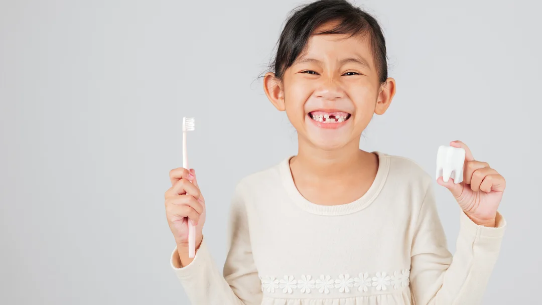 A young patient smiling at Lake County Dental, holding a toothbrush and a model tooth